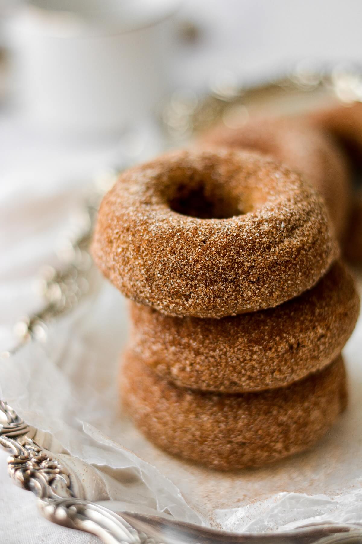 Pumpkin donuts, coated in cinnamon sugar, stacked on a silver plate.