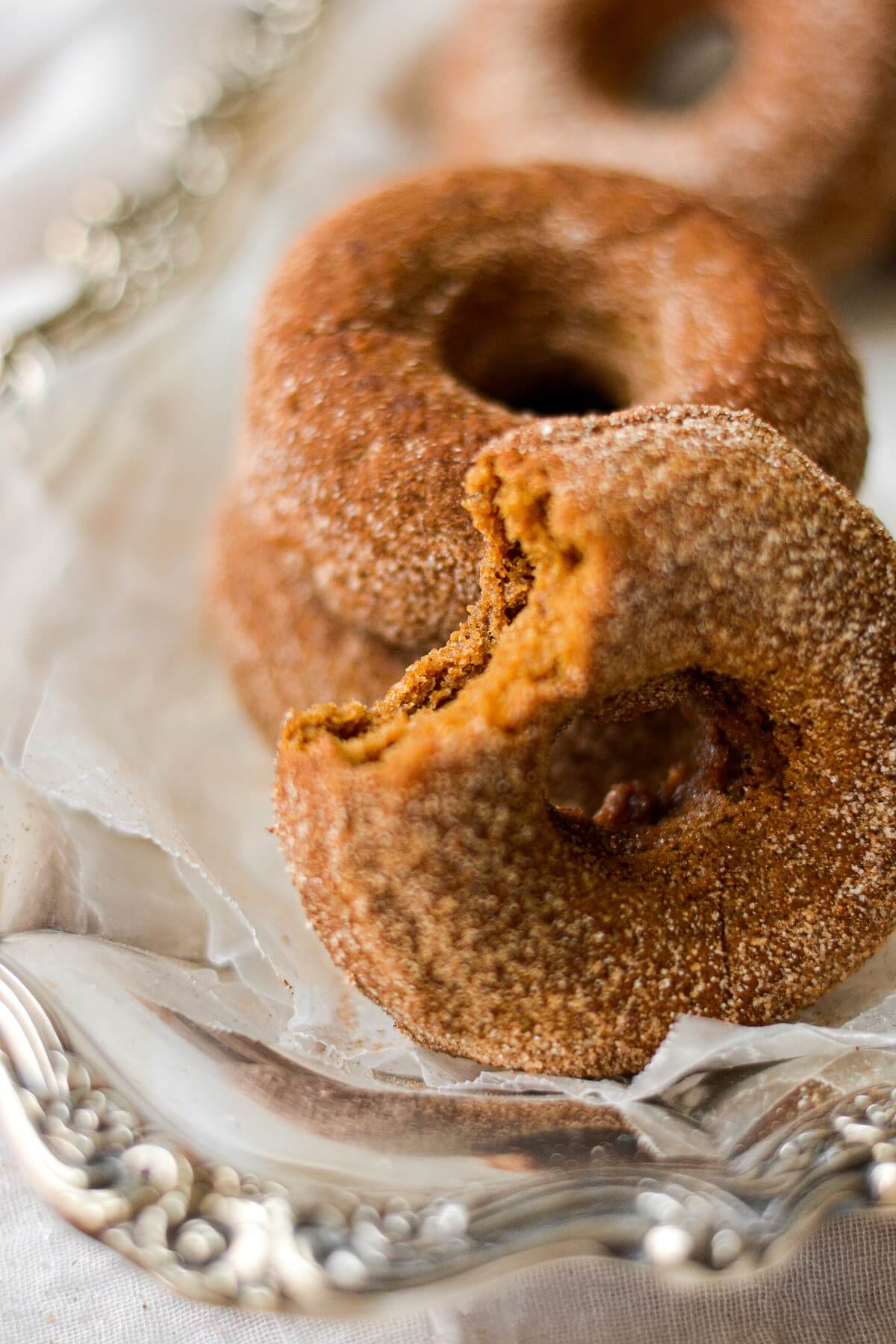 Closeup of baked pumpkin spice donuts, coated in cinnamon sugar, one with a bite taken out of it.