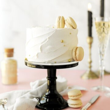 Toasted sugar champagne cake on a black cake stand, with candles, macarons and glasses of champagne.