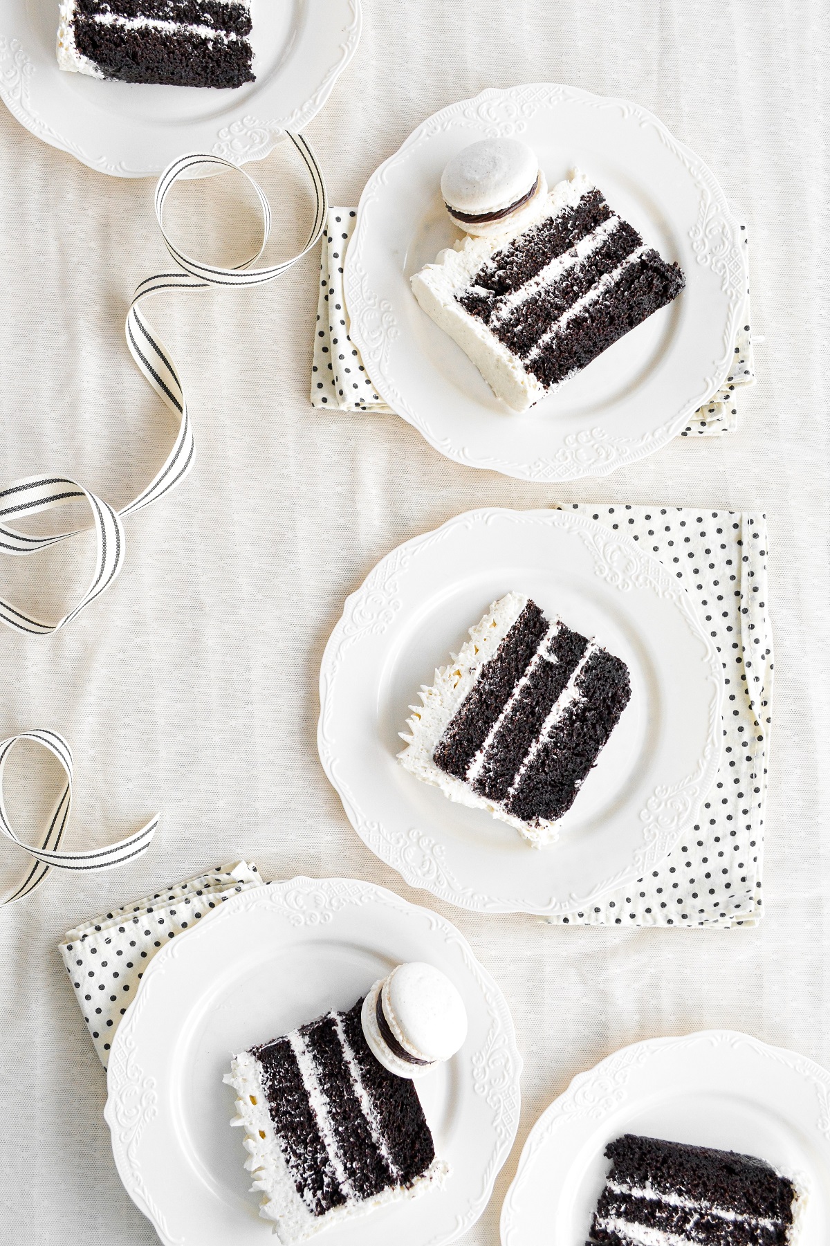 Five pieces of chocolate cake with vanilla buttercream, on white plates.