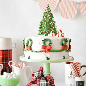 A Christmas cake with a candy tree topper with sprinkles, peppermints and buttercream wreaths piped around the sides.