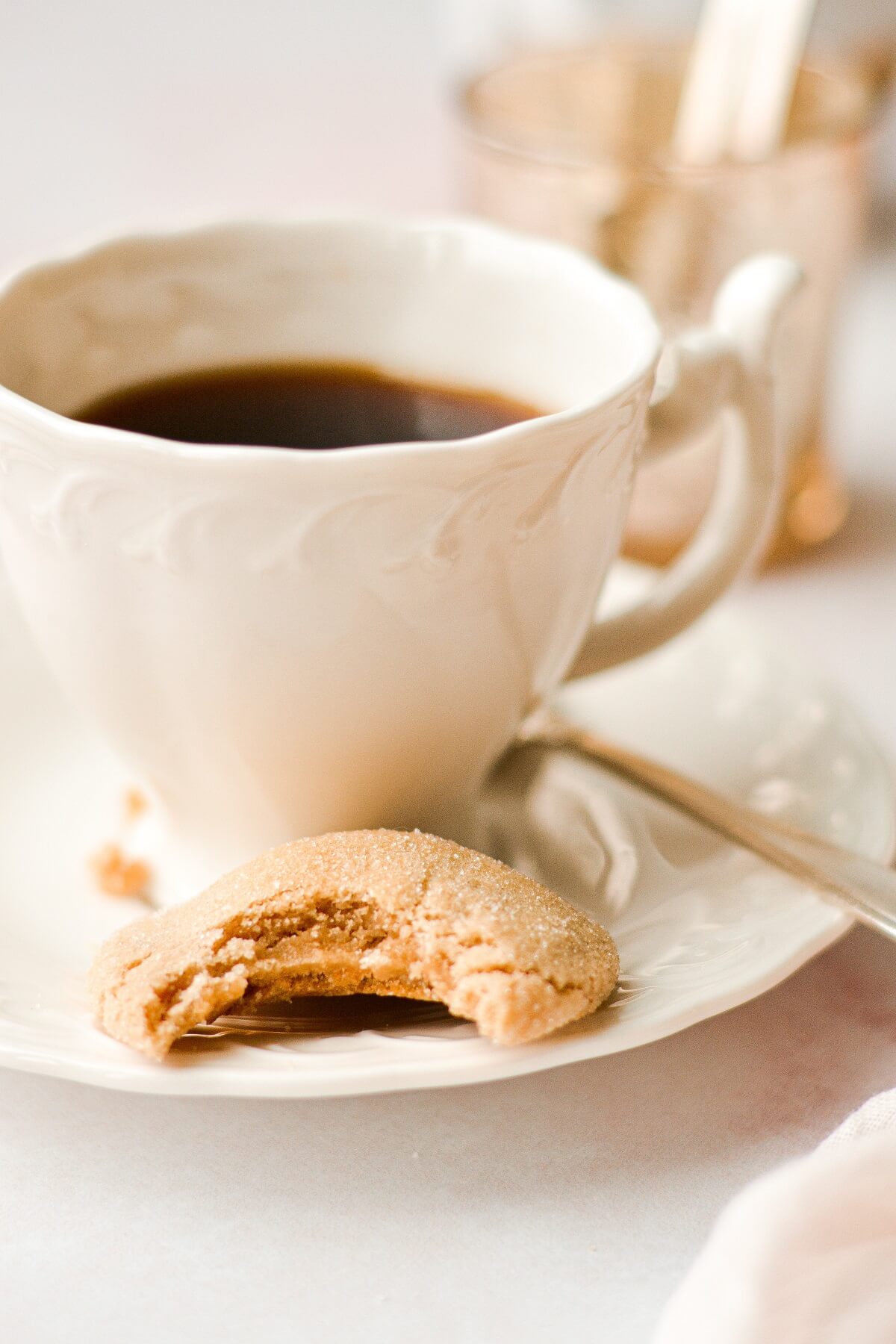 A half eaten maple cookie next to a cup of coffee.