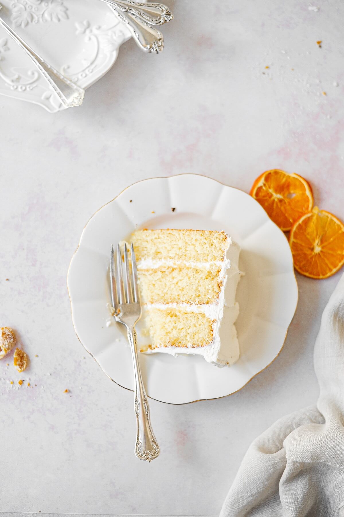 A slice of orange layer cake on a white plate, with dried orange slices scattered around.