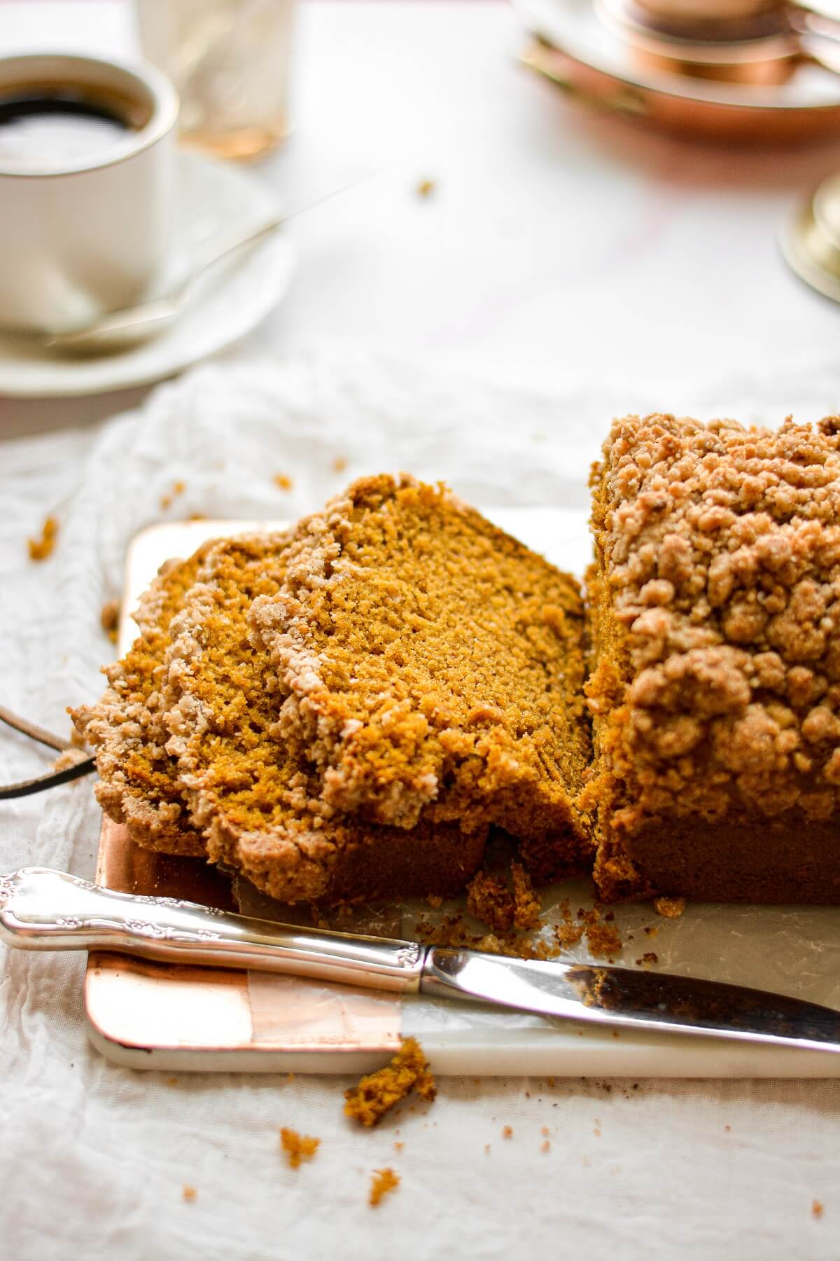 A loaf of pumpkin streusel bread, with a few pieces sliced on a cutting board.