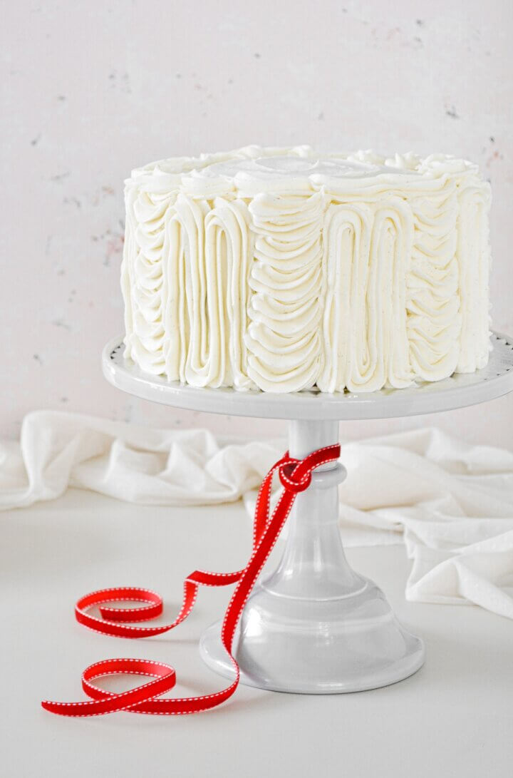 Red velvet cake on a light gray cake stand, with a red ribbon tied around the cake stand.