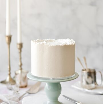 White velvet cake on a sage green cake stand, with taper candles in the background.