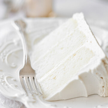 A slice of white velvet cake on a white plate, with a silver fork..