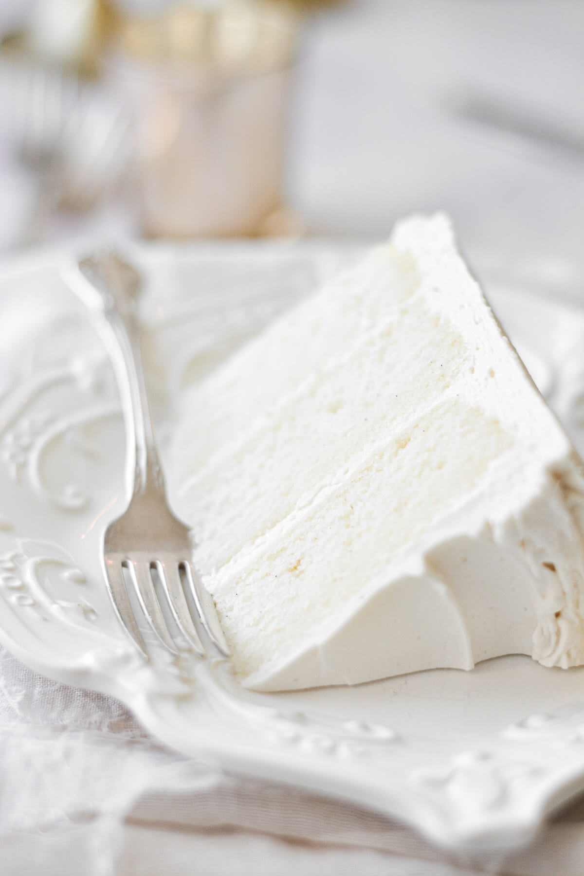 A slice of white velvet cake on a white plate, with a silver fork..