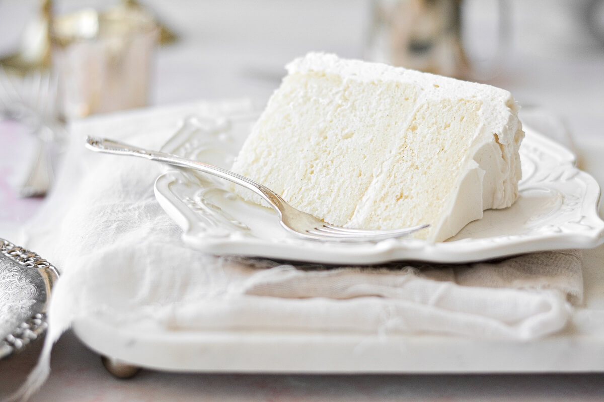 A slice of white velvet cake on a white plate, with a silver fork..