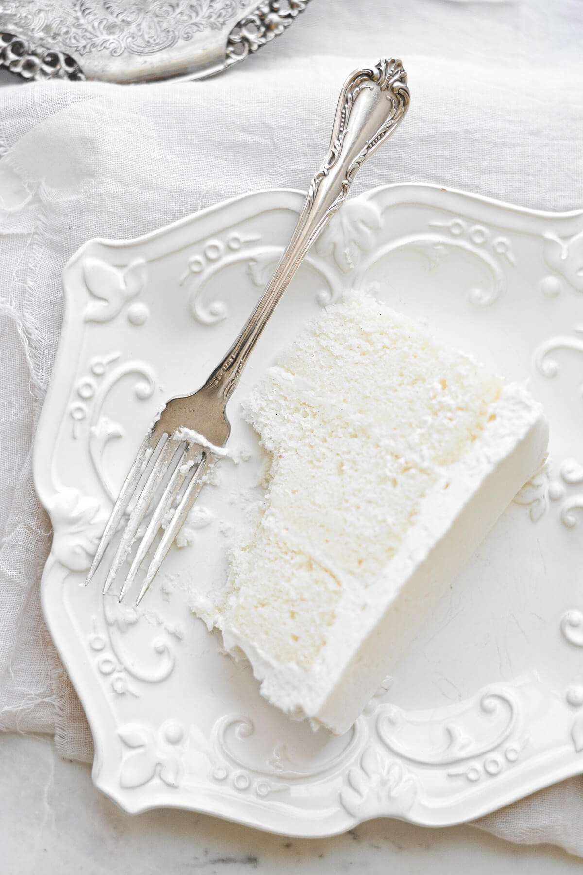 A slice of white velvet cake with a bite taken out of it, on a white plate, with a silver fork..