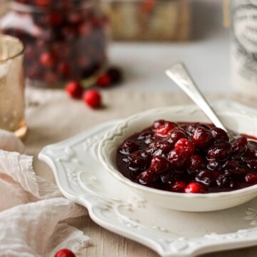 Homemade cranberry sauce in a white bowl, with a jar of cranberries in the background.