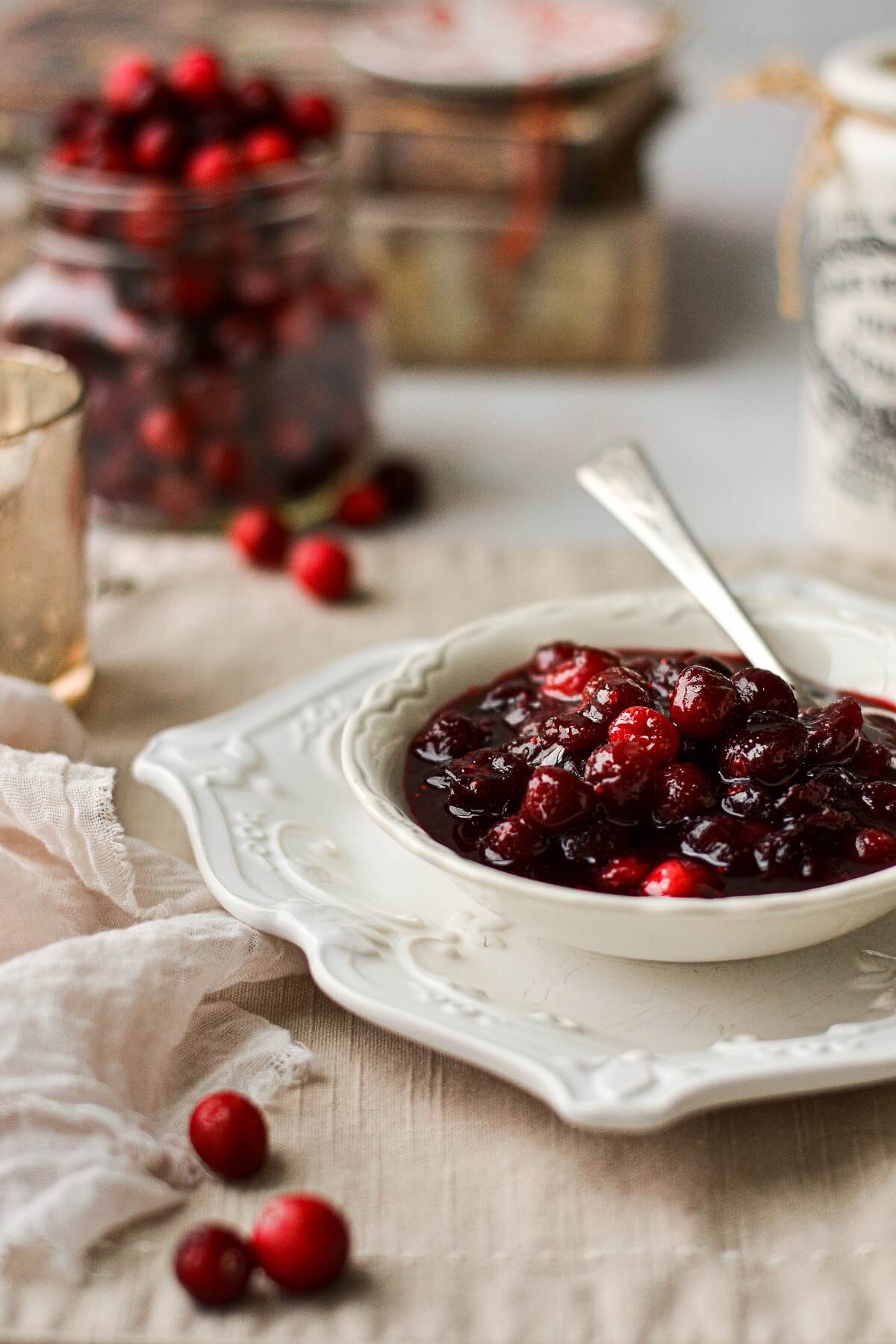 Homemade cranberry sauce in a white bowl, with a jar of cranberries in the background.