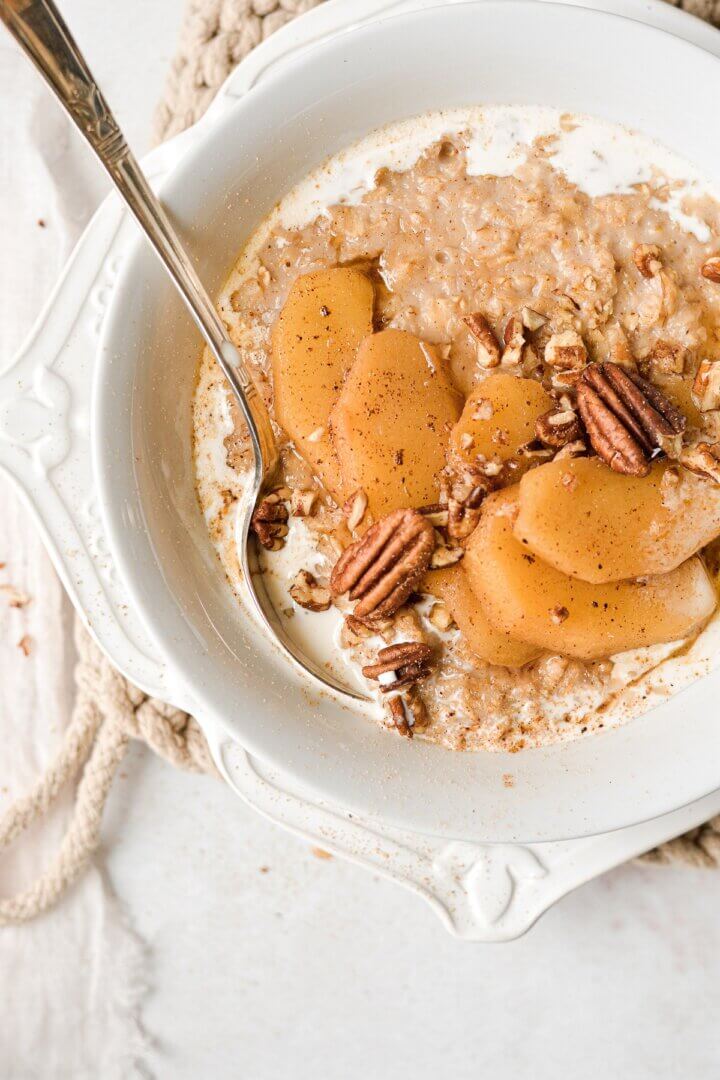 A bowl of maple cinnamon oatmeal, topped with sliced apples and pecans.