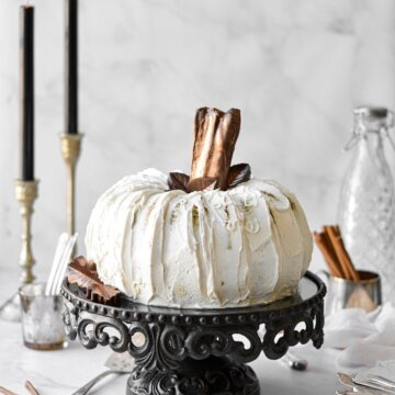 A white pumpkin cake with chocolate leaves and chocolate covered pretzel stem.