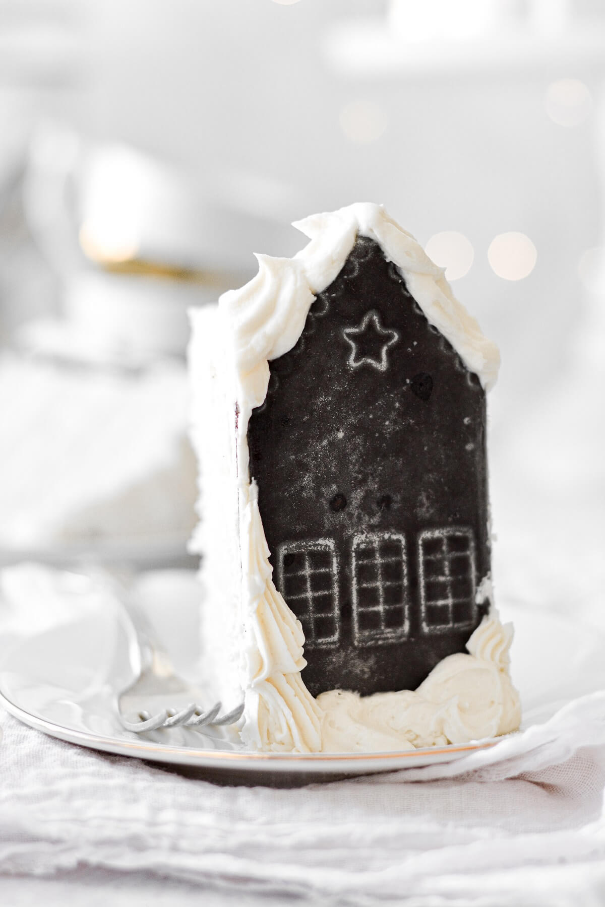 A slice of white velvet cake, with an iced chocolate shortbread cookie decorated like a house for Christmas.