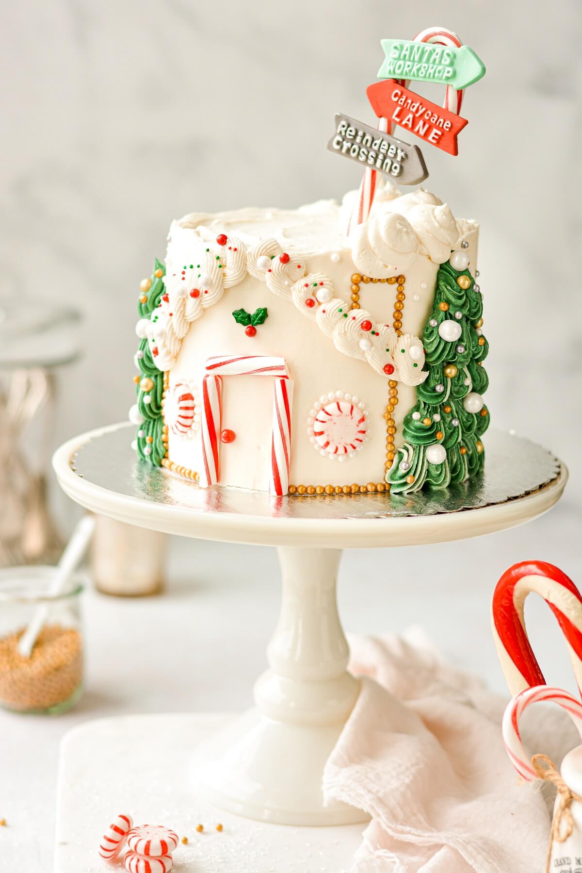 A Christmas cake decorated like Santa's workshop, and topped with a candy cane street sign.