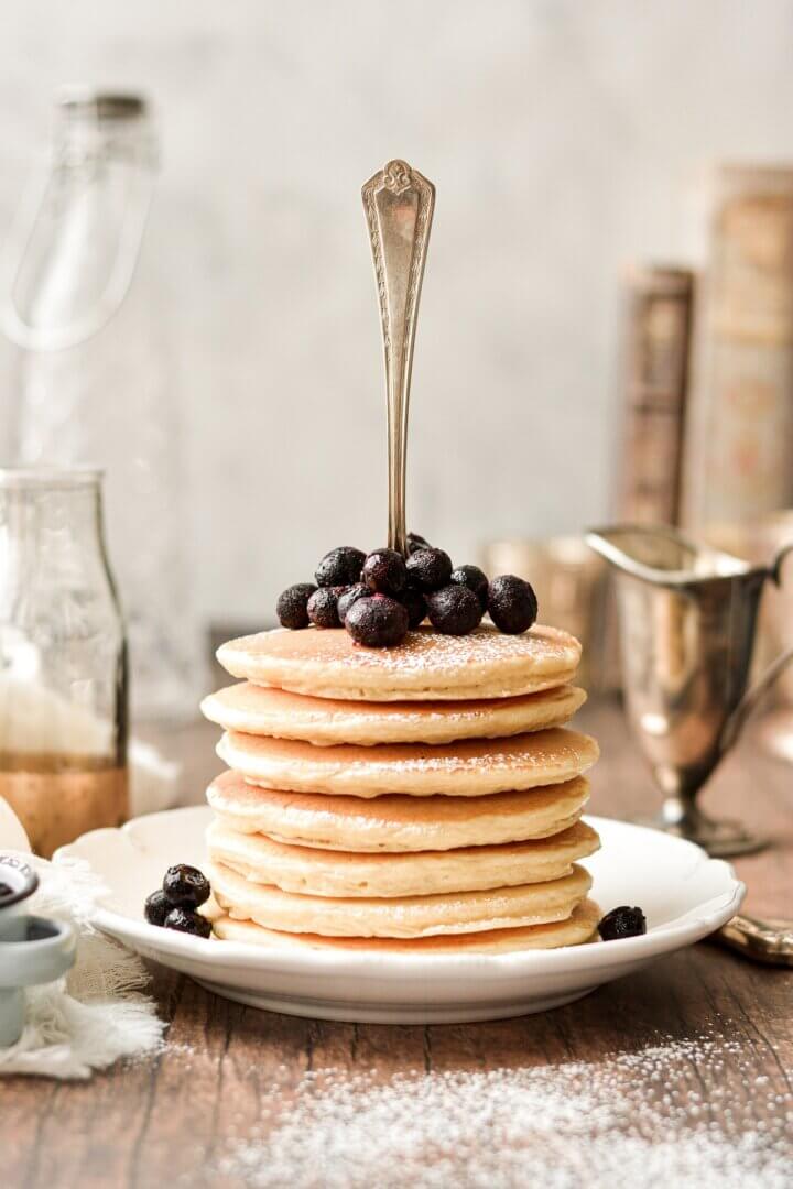 A stack of the best classic pancakes, topped with blueberries, and a fork sticking in the top.