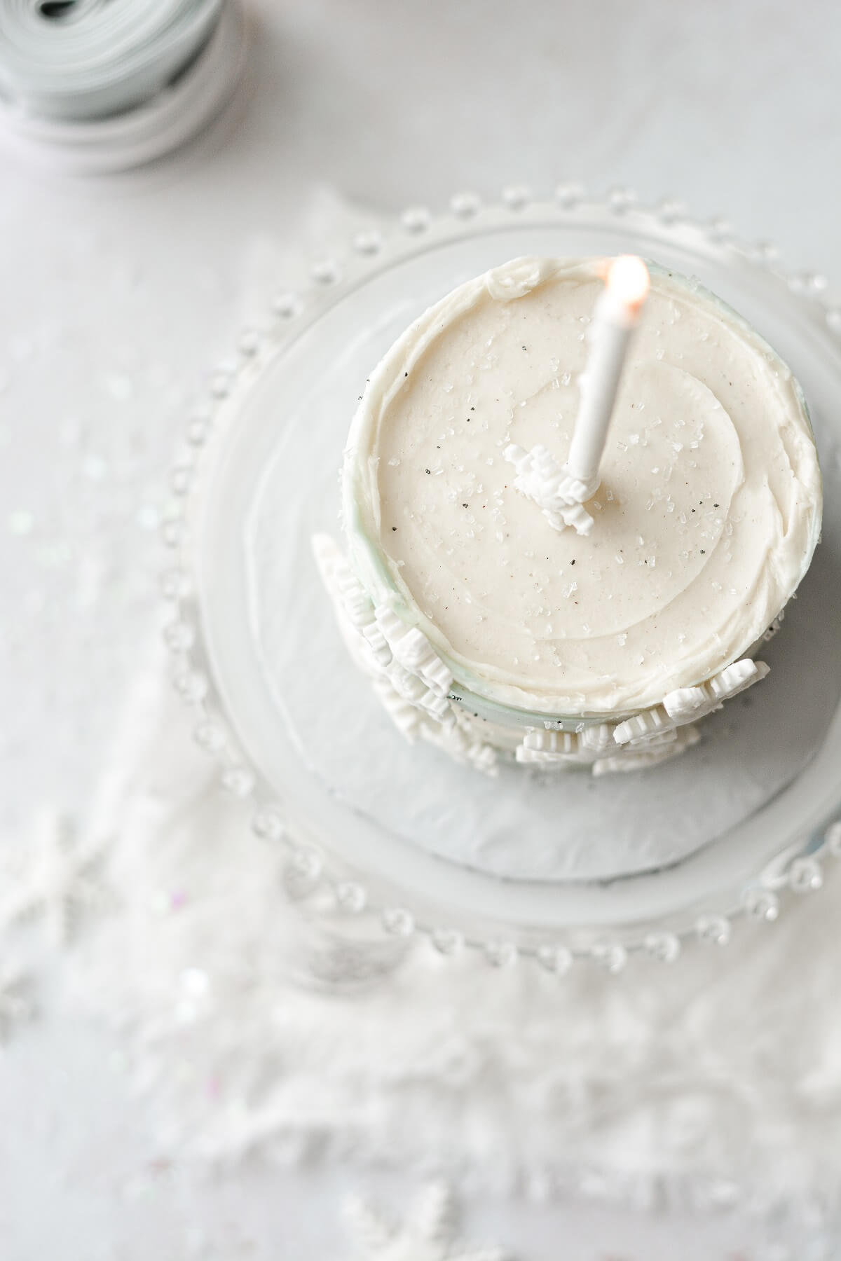 Top of a light blue and white snowflake cake with a white birthday candle.