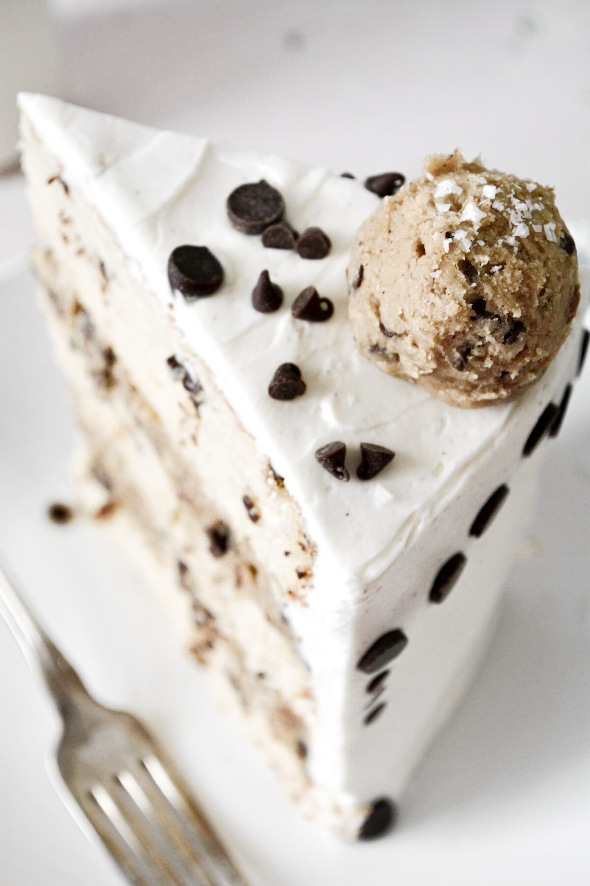 A slice of chocolate chip cookie dough cake, decorated with chocolate chips and balls of cookie dough.