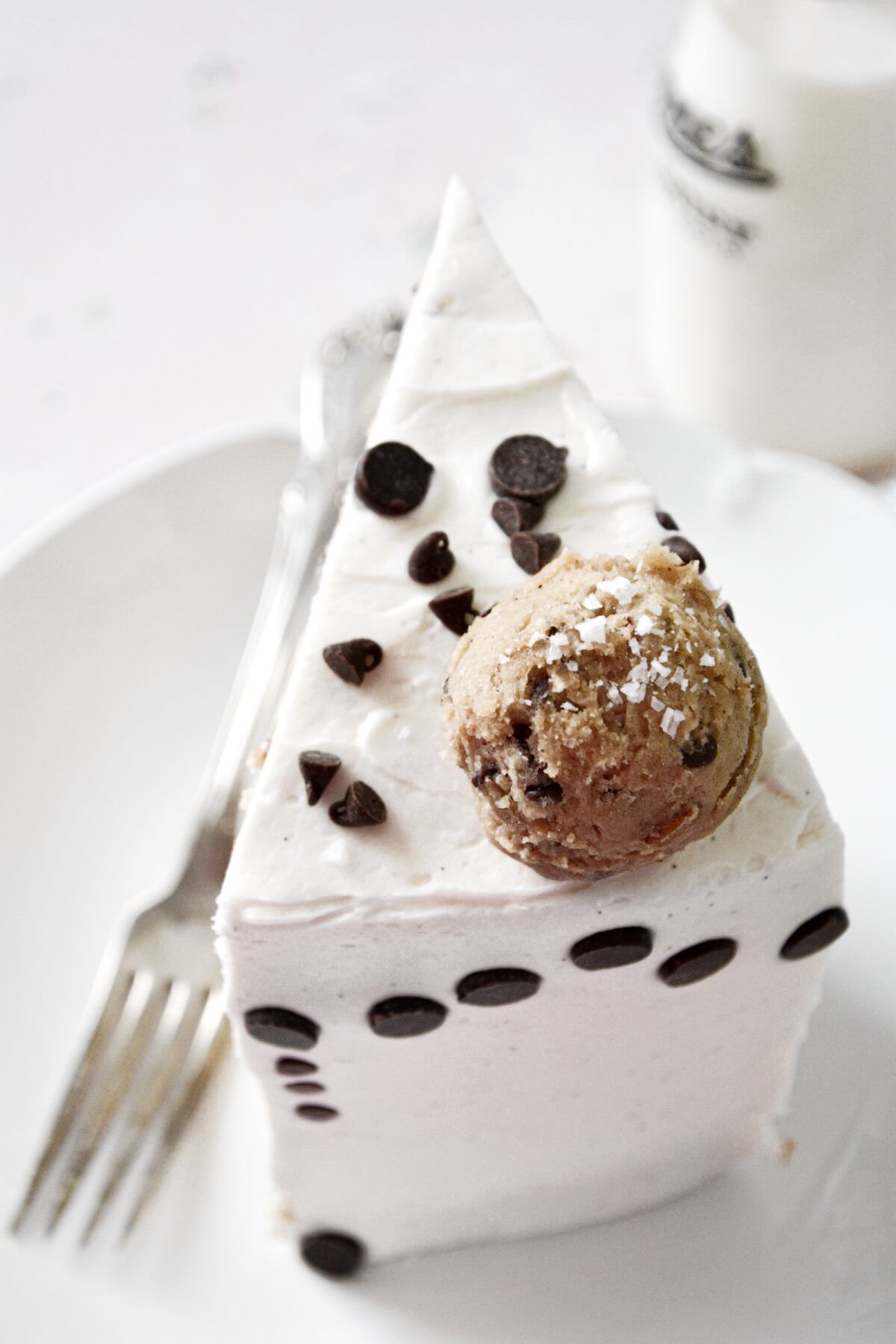 A slice of chocolate chip cookie dough cake, decorated with chocolate chips and balls of cookie dough.