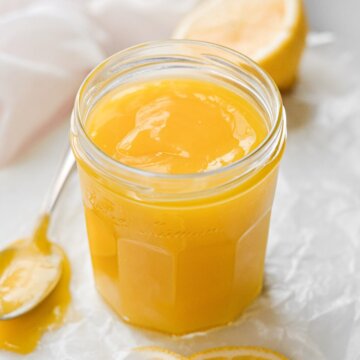 A jar of homemade lemon curd with lemon slices scattered around.