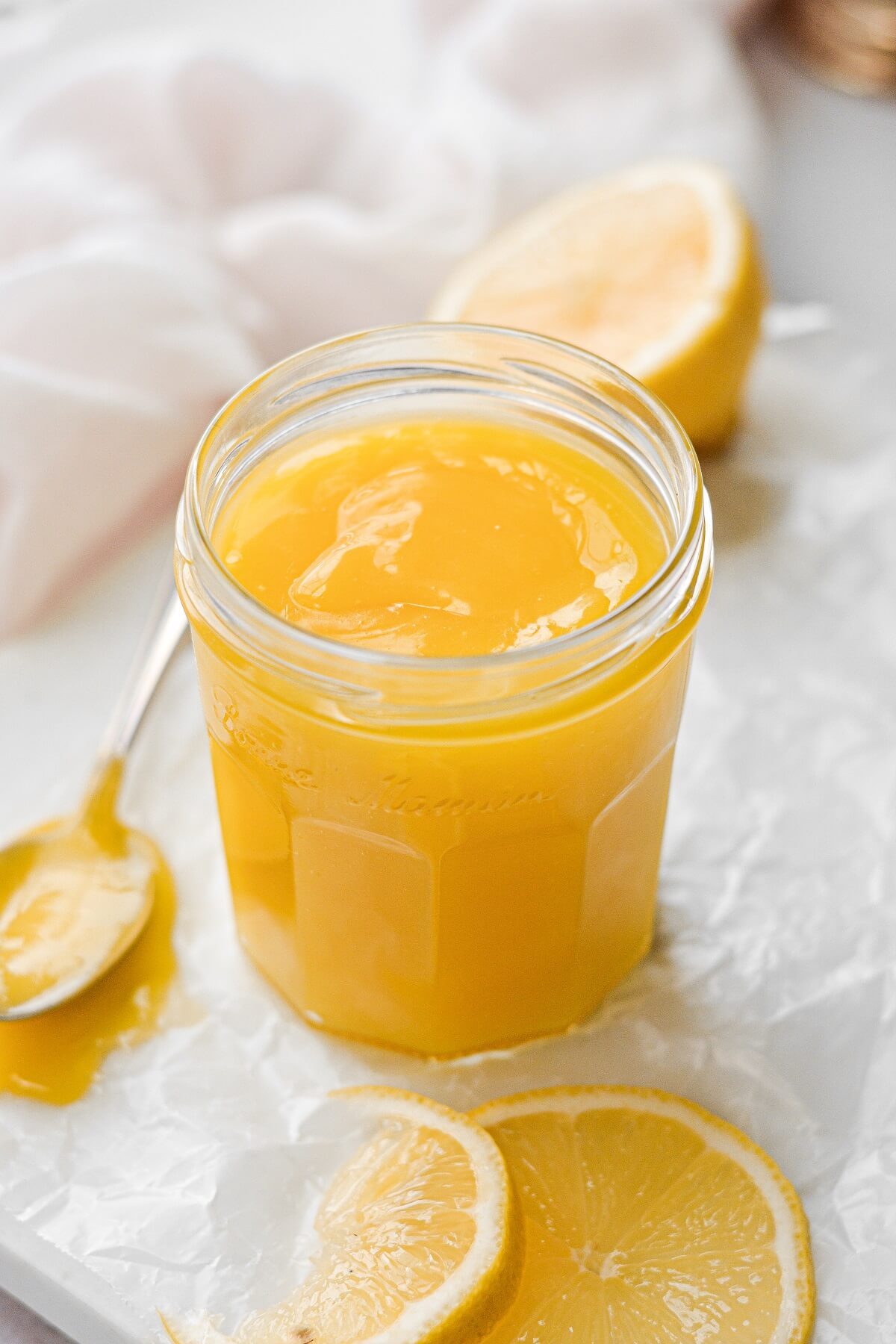 A jar of homemade lemon curd with lemon slices scattered around.