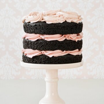 Naked chocolate cake with pink buttercream on a pink cake stand.