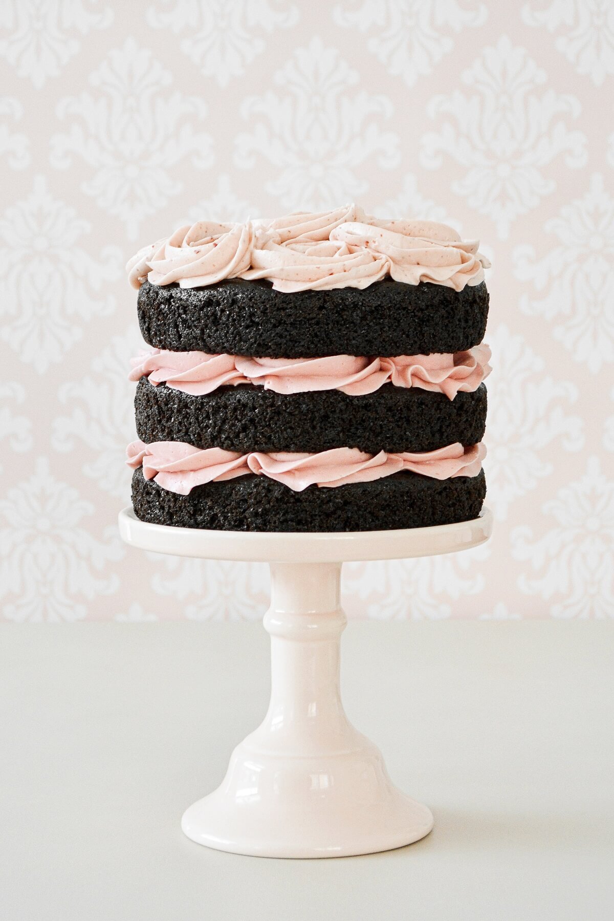 A naked chocolate cake with piped raspberry buttercream rosettes.