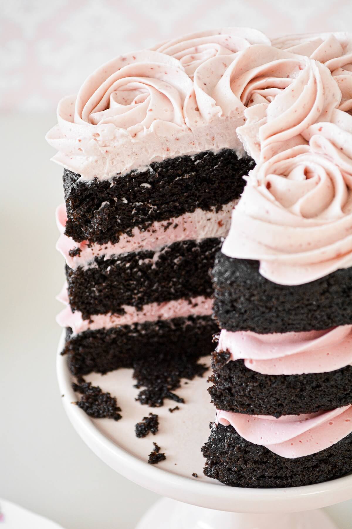 A naked chocolate cake with piped raspberry buttercream rosettes, and one slice cut.