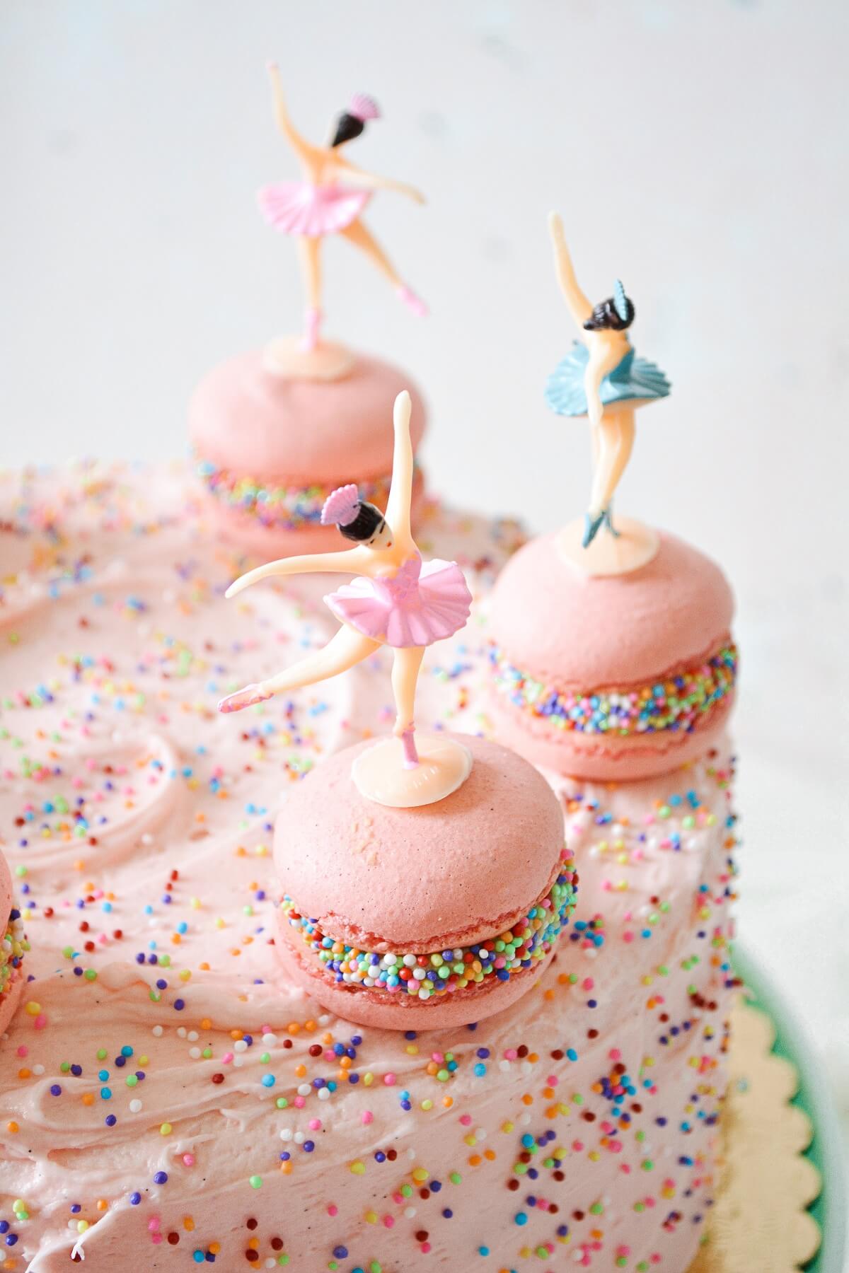A pink sprinkles cake with French macarons and ballerina cake toppers.