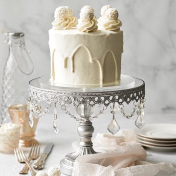 A white chocolate cake with drip and white chocolate truffles, on a silver mirrored cake stand.