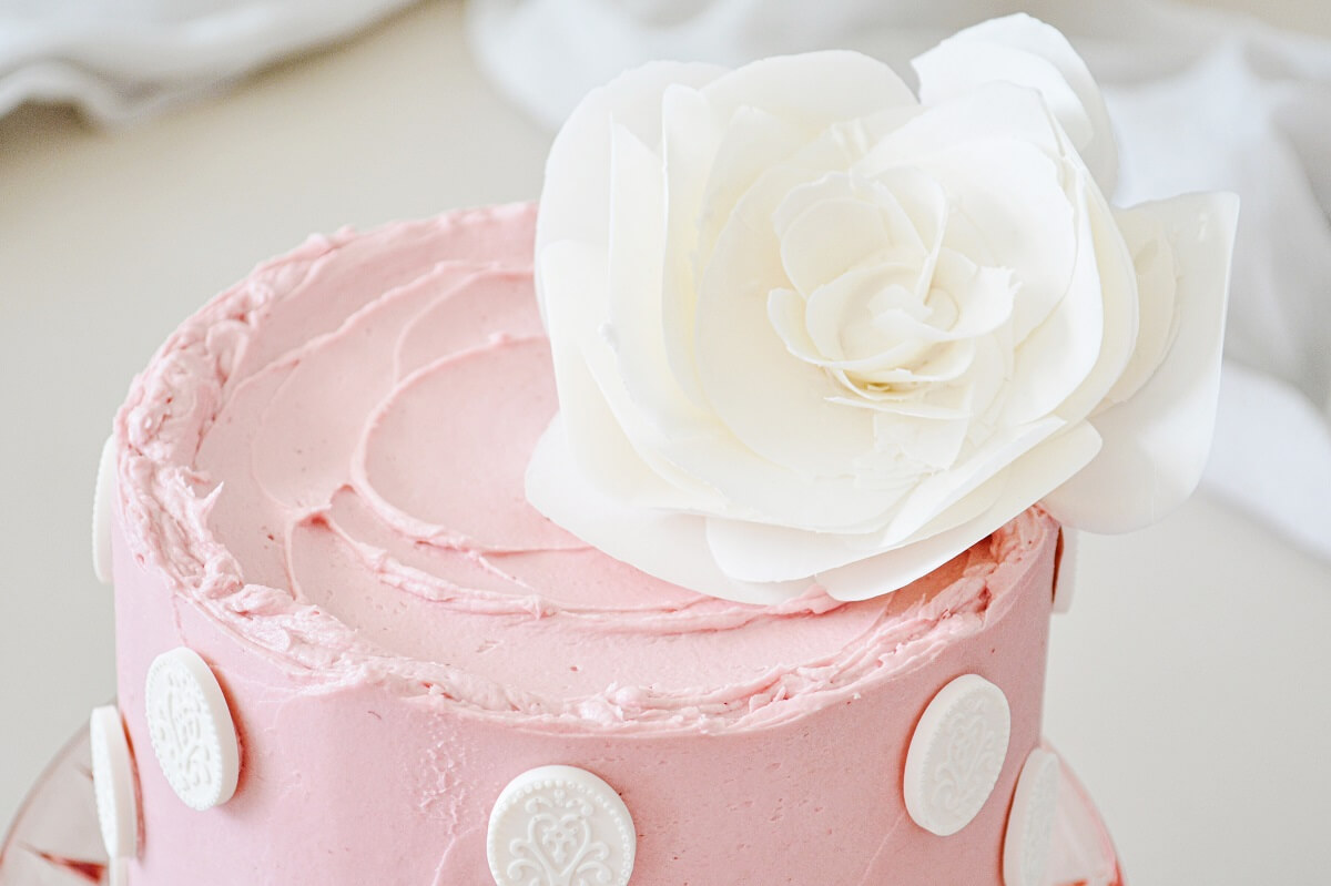 Lemon raspberry cake on a pink cake pedestal, topped with a white chocolate flower.