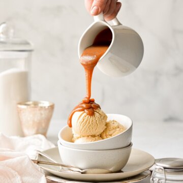A jar of salted caramel sauce, pouring onto a bowl of salted caramel ice cream.