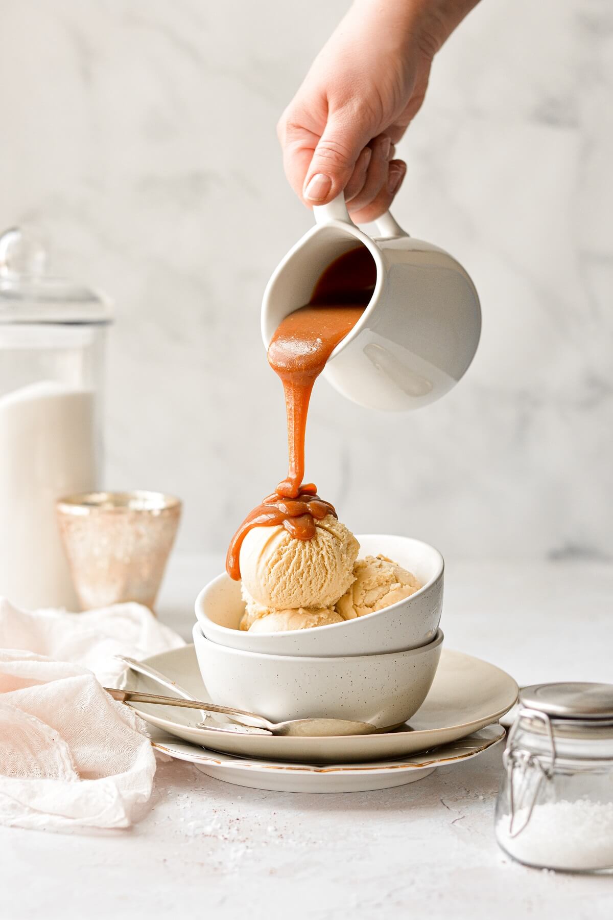 A jar of salted caramel sauce, pouring onto a bowl of salted caramel ice cream.