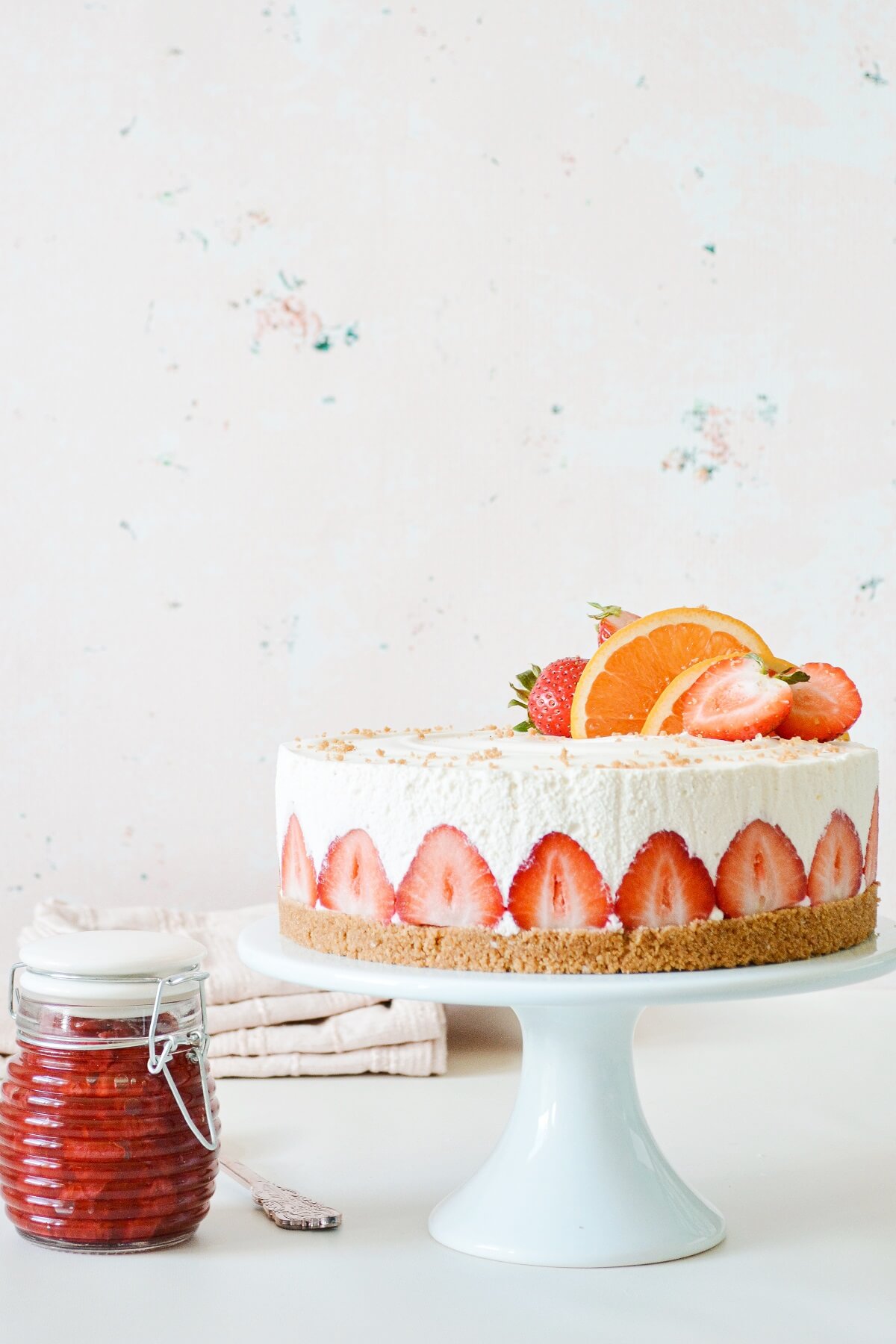 Strawberry orange cheesecake, lined with sliced strawberries, next to a jar of strawberry sauce.