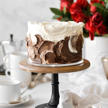 Vanilla latte cake with swirls of vanilla and chocolate espresso buttercream, next to a vase of red roses.