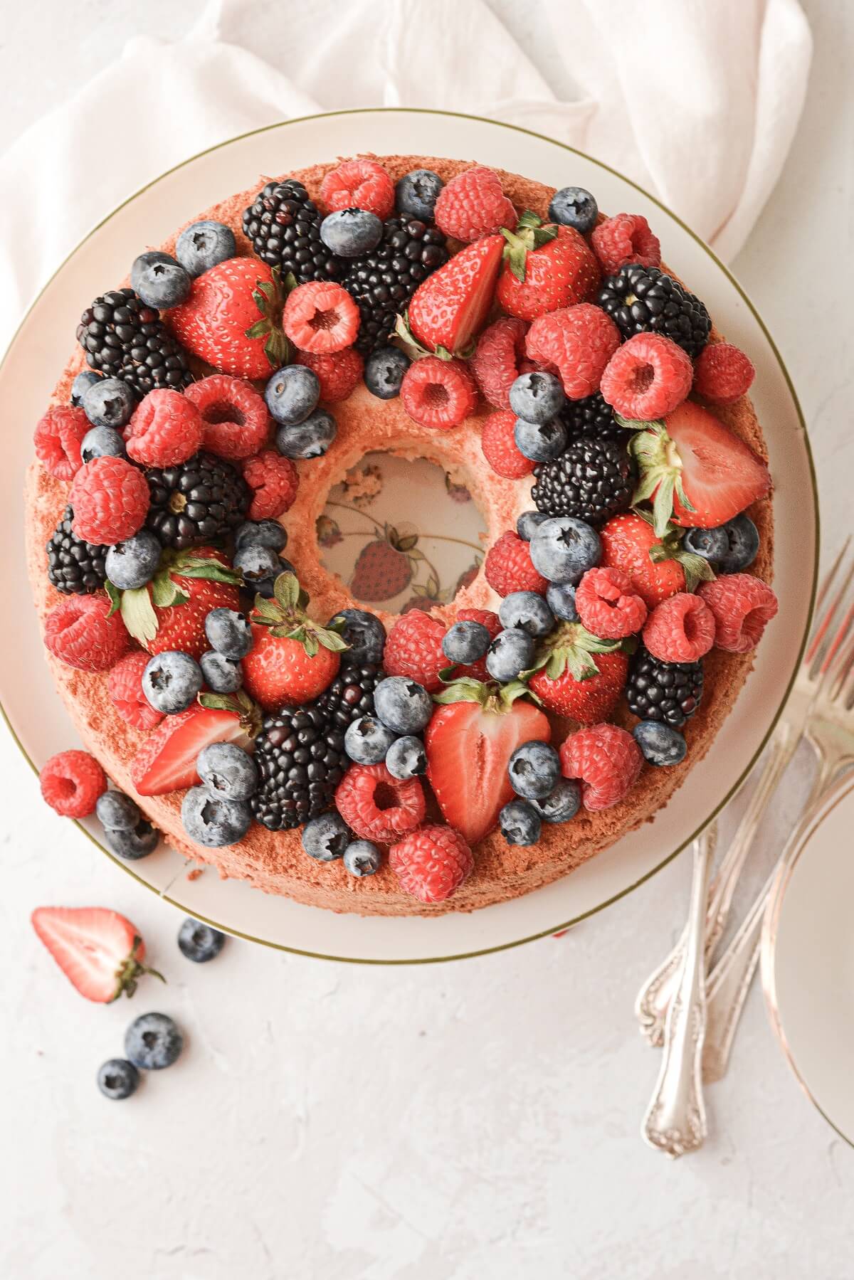 Angel food cake on a vintage cake stand, topped with assorted berries.