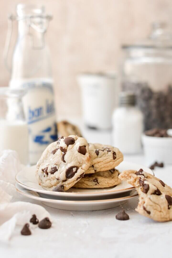 High altitude chocolate chip cookies, on a plate, with jars of milk.