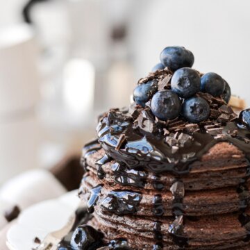Chocolate pancakes topped with chocolate syrup, chopped chocolate and blueberries.