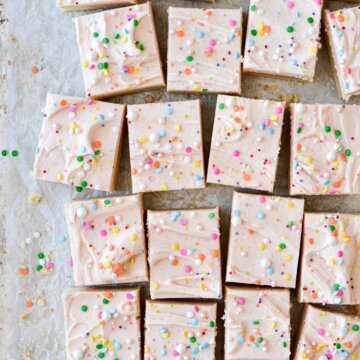 Soft frosted sugar cookie bars, cut into squares, with pale pink frosting and sprinkles.