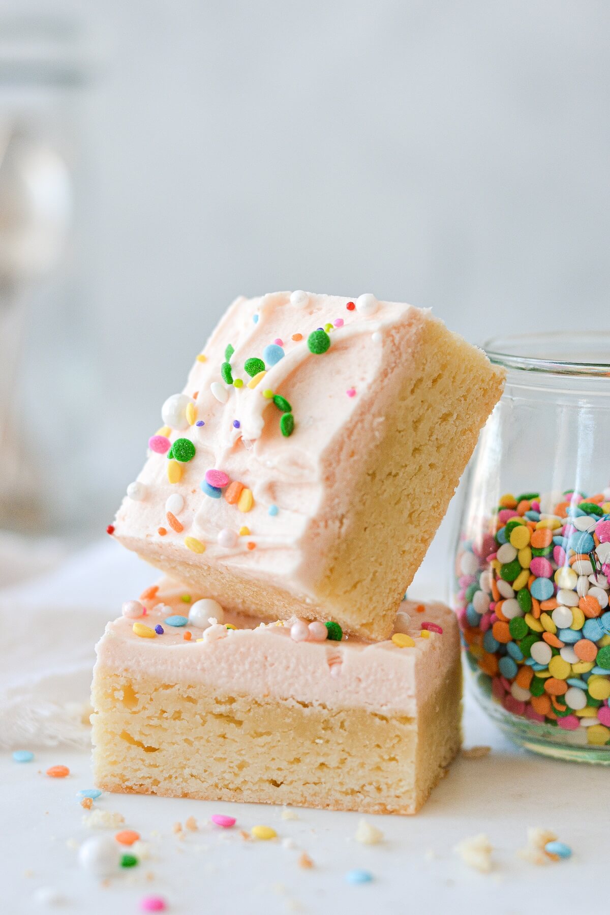 Soft frosted sugar cookie bars, cut into squares, with pale pink frosting and sprinkles.