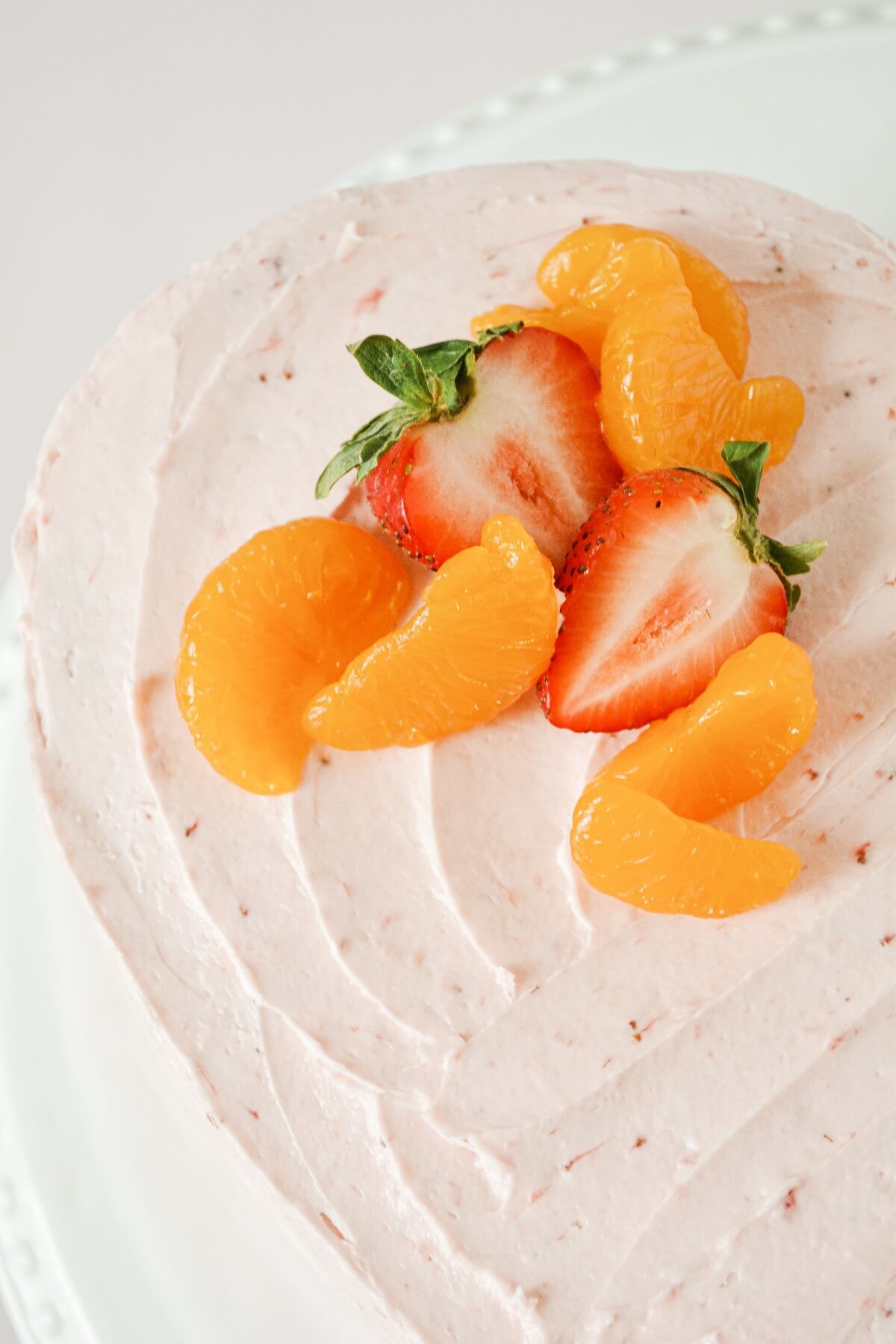 Heart shaped strawberry orange cake, topped with sliced strawberries and mandarin oranges.