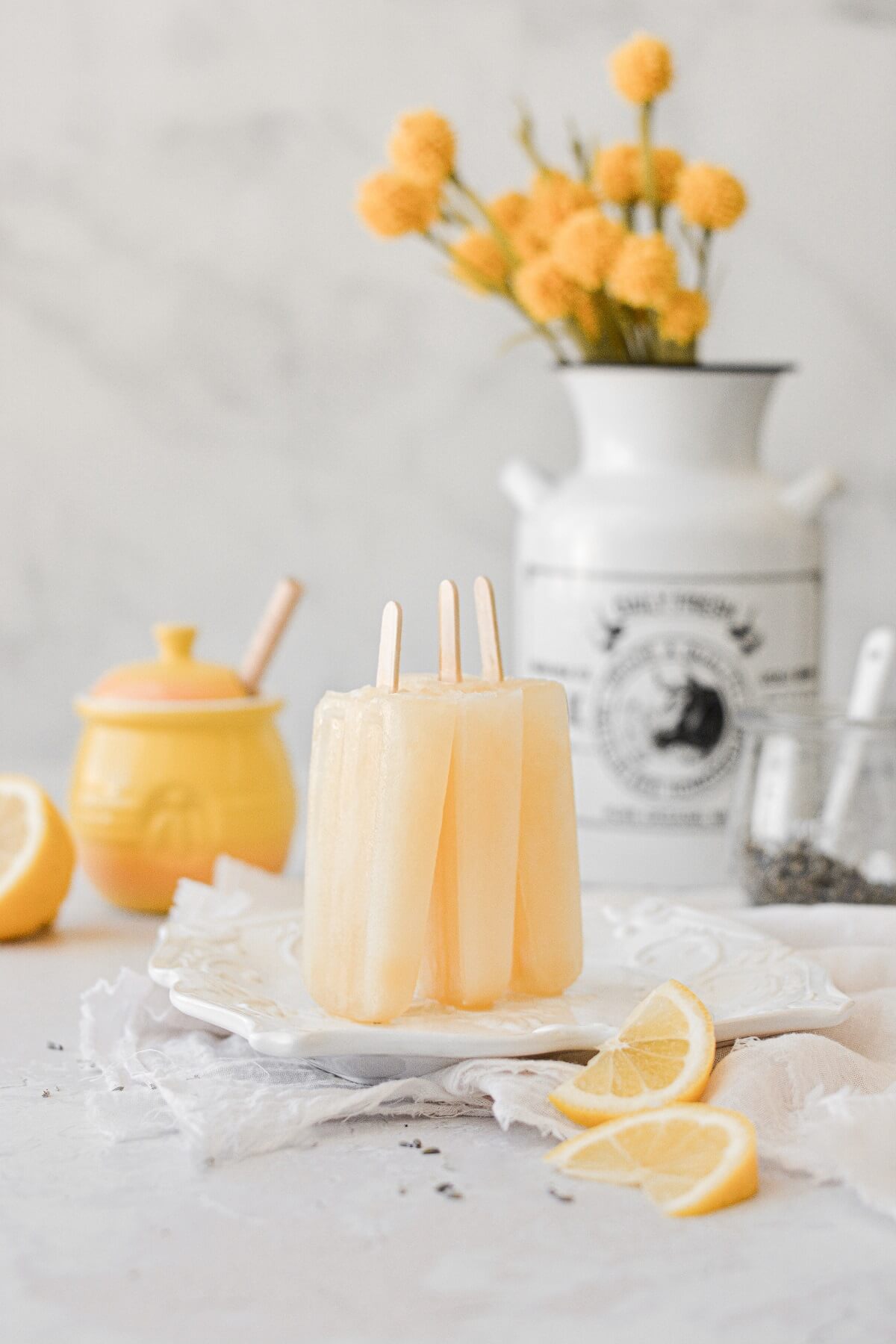 Lavender lemonade honey popsicles, propped against each other on a white plate.