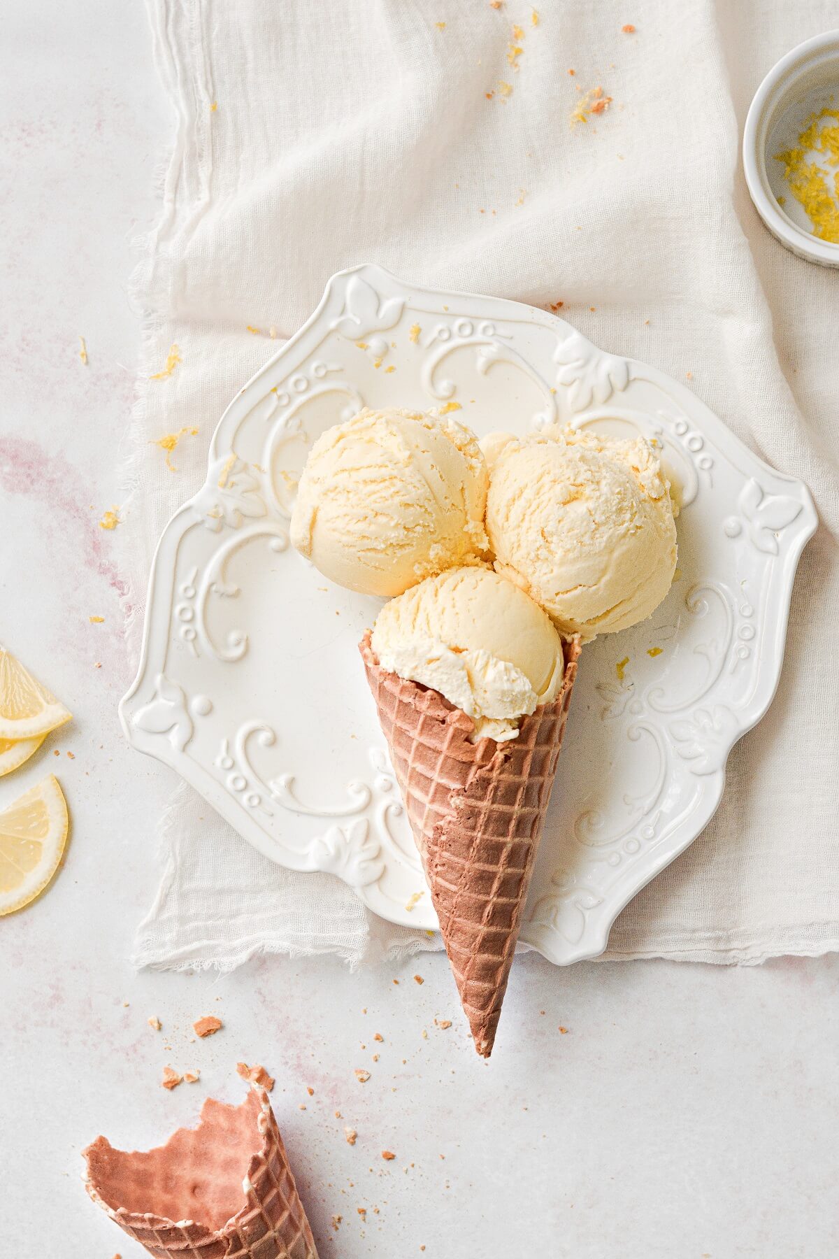 Scoops of lemon ice cream in a waffle cone, on a white plate.