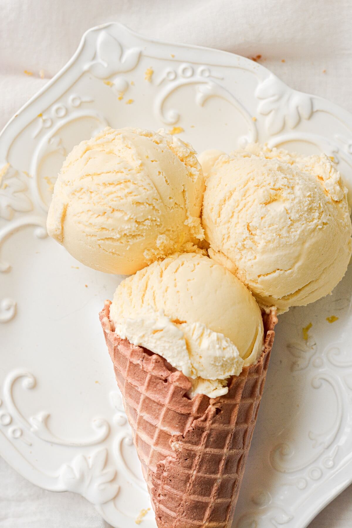 Scoops of lemon ice cream in a waffle cone, on a white plate.