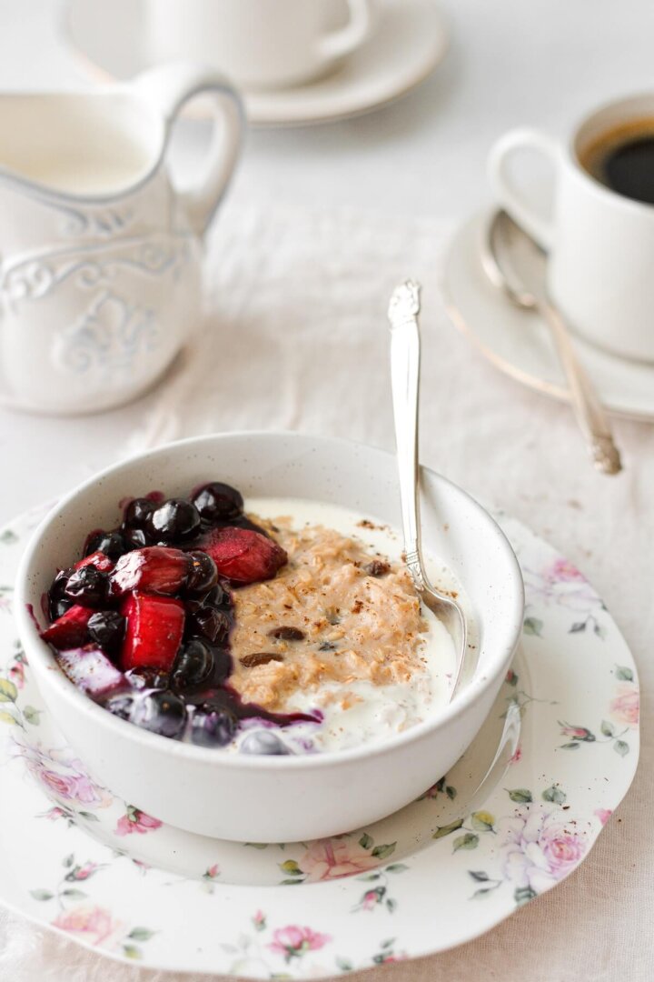 A bowl of oatmeal topped with blueberry rhubarb compote, with cups of coffee.