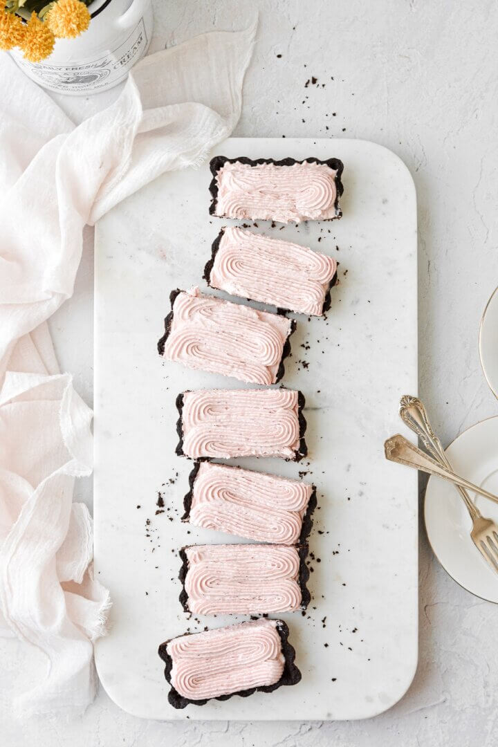 Strawberry rhubarb cream tart with a chocolate shortbread crust, cut into slices on a marble slab.