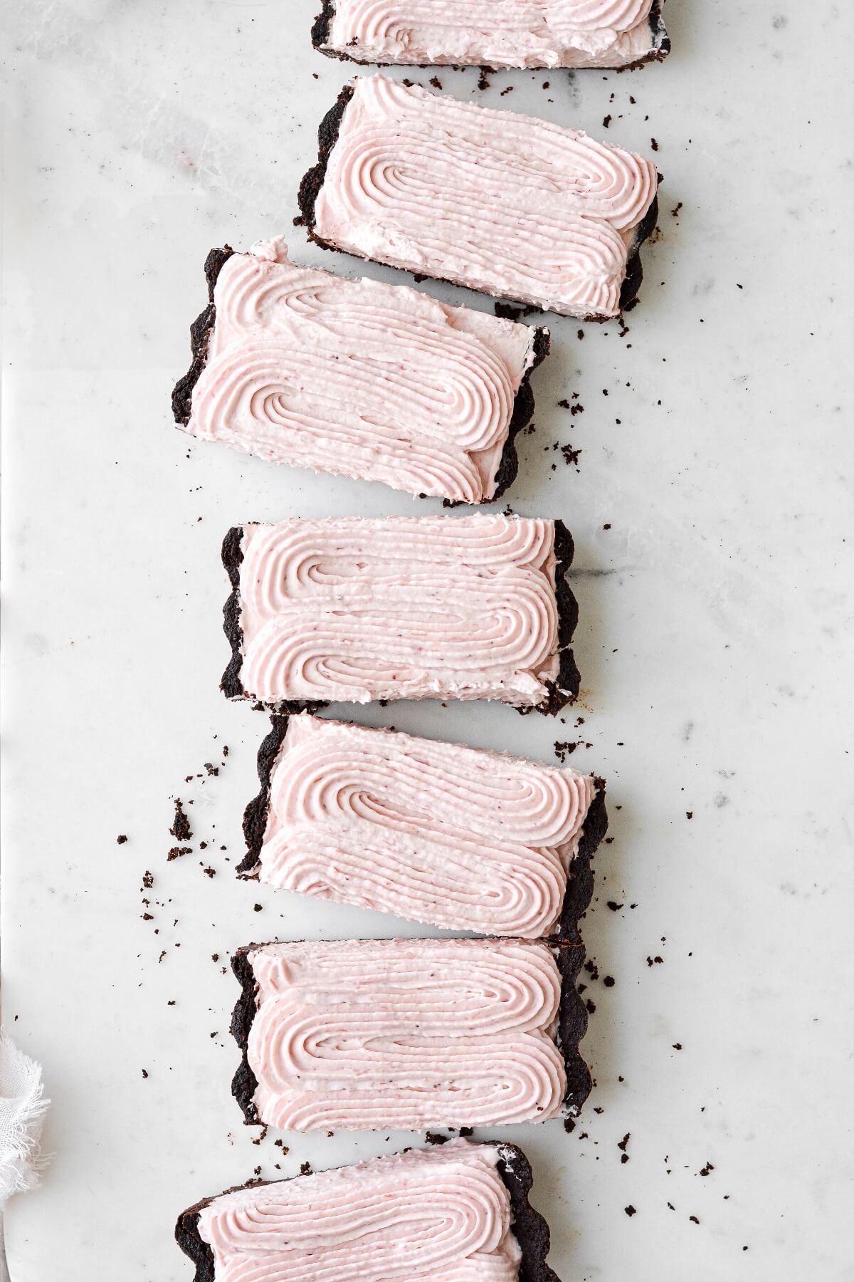 Strawberry rhubarb cream tart with a chocolate shortbread crust, cut into slices on a marble slab.
