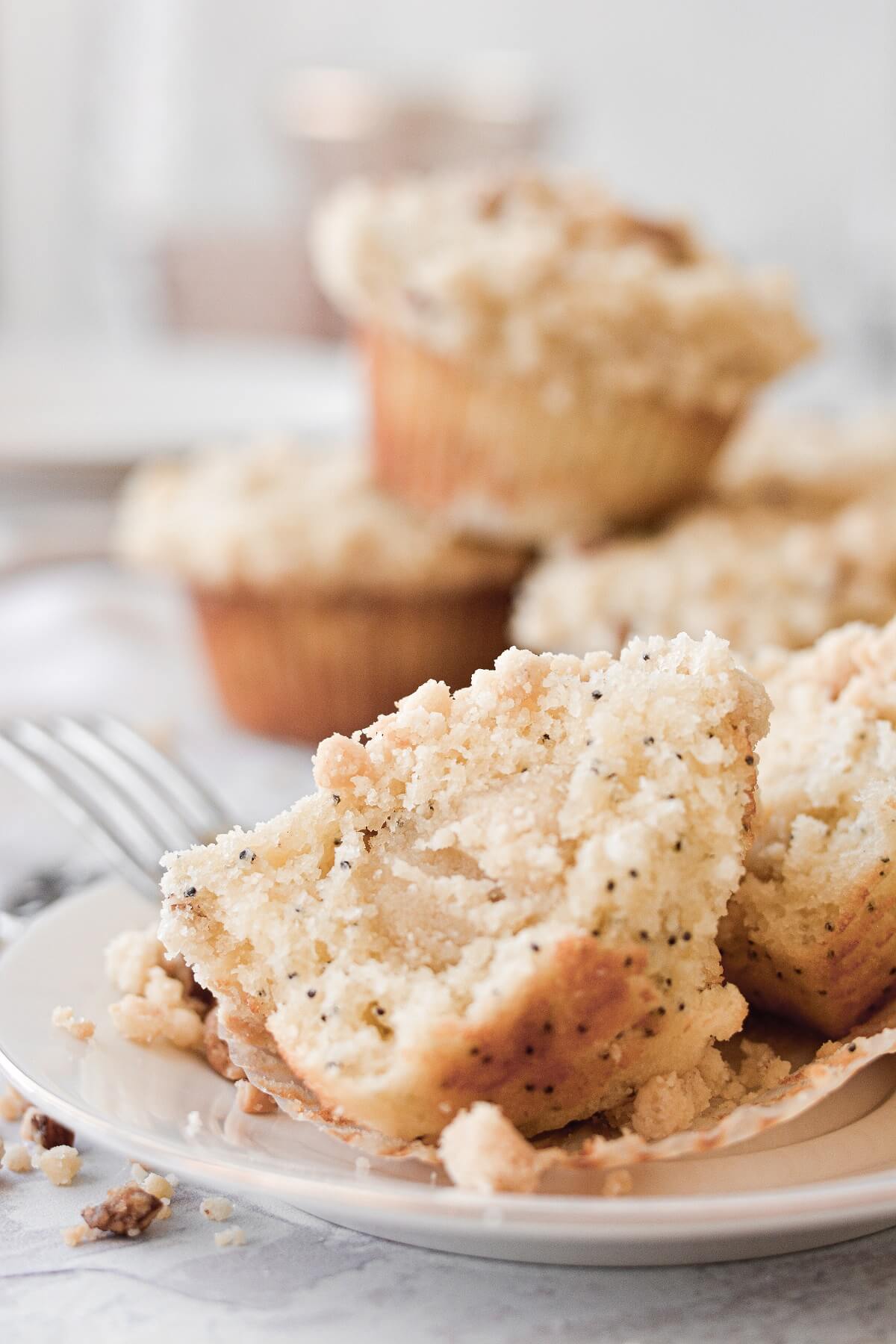 Almond poppy seed muffins, piled on top of a cooling rack, with one muffin split open.