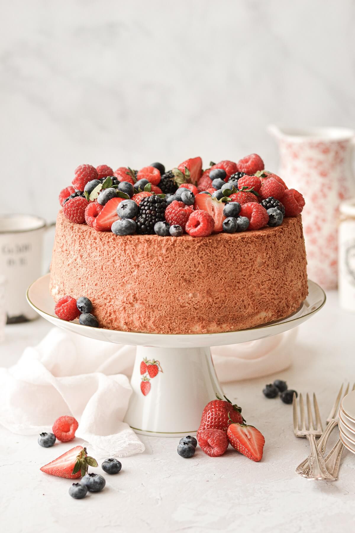 Angel food cake on a vintage cake stand, topped with assorted berries.